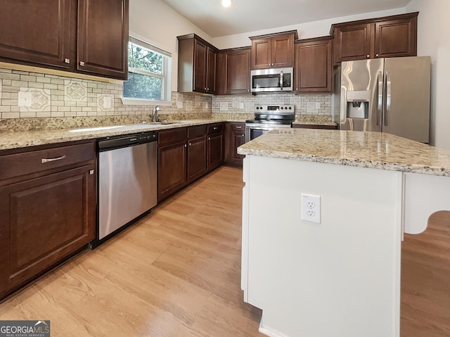 kitchen with light stone countertops, stainless steel appliances, light hardwood / wood-style flooring, decorative backsplash, and a kitchen island