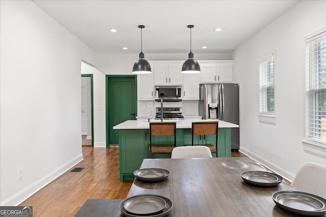 kitchen featuring hanging light fixtures, stainless steel appliances, a center island, white cabinets, and a kitchen bar