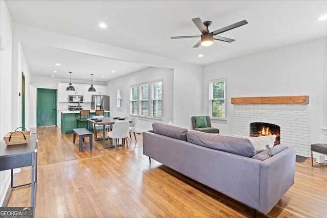 living room featuring a brick fireplace, ceiling fan, and light hardwood / wood-style flooring