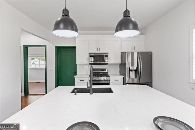 kitchen featuring pendant lighting, stainless steel appliances, light stone counters, and white cabinets