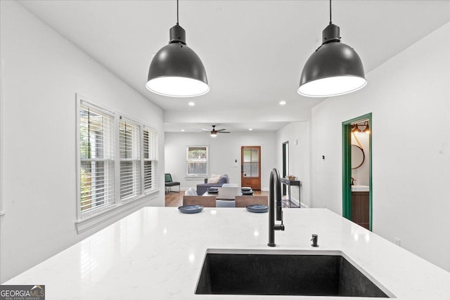 kitchen with light stone counters, sink, and hanging light fixtures