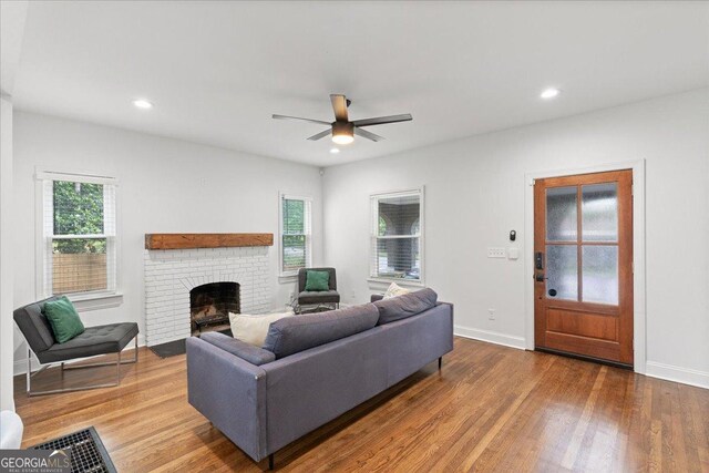 living room featuring hardwood / wood-style flooring, ceiling fan, and a brick fireplace