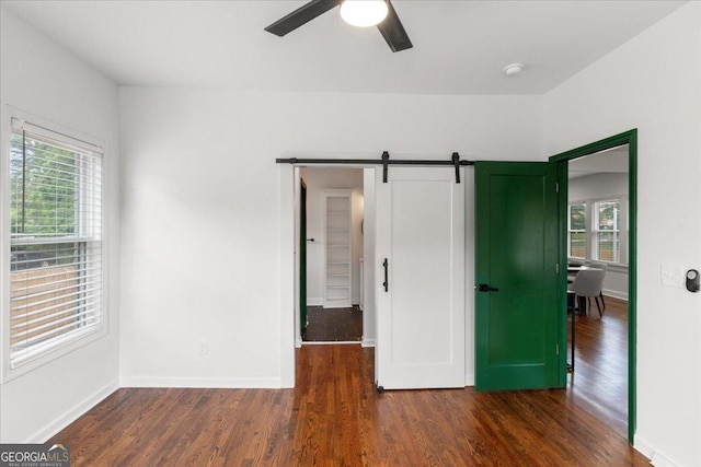 unfurnished bedroom with dark wood-type flooring, ceiling fan, and a barn door