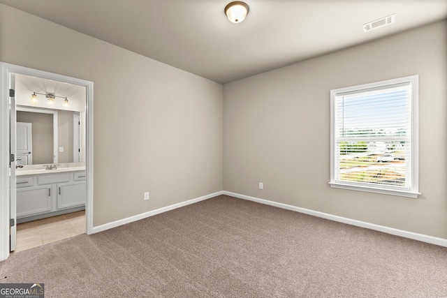 unfurnished bedroom with ensuite bathroom, light colored carpet, and sink