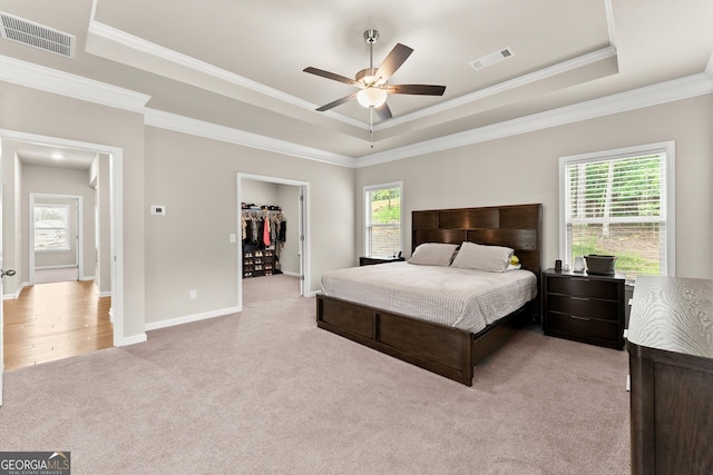 bedroom featuring ceiling fan, a raised ceiling, crown molding, light colored carpet, and a walk in closet