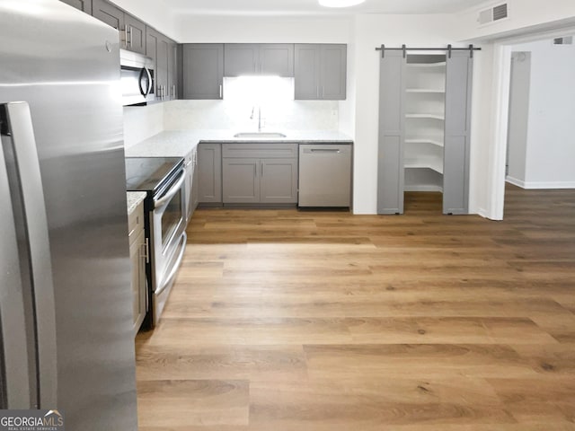 kitchen featuring appliances with stainless steel finishes, a barn door, light hardwood / wood-style floors, and sink