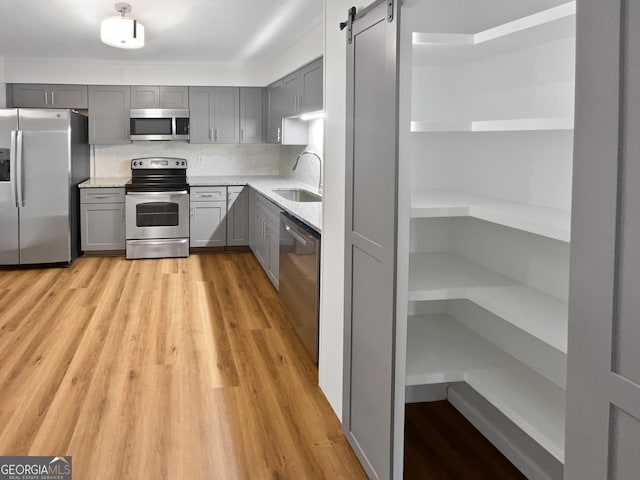 kitchen featuring decorative backsplash, appliances with stainless steel finishes, gray cabinetry, sink, and a barn door