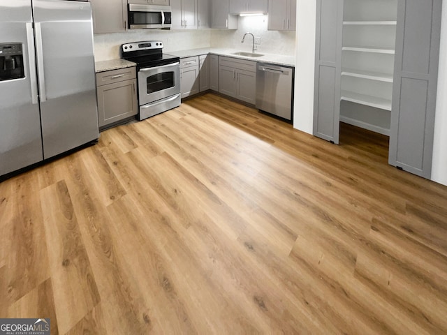 kitchen with gray cabinetry, sink, stainless steel appliances, tasteful backsplash, and light hardwood / wood-style floors