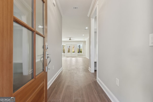 hall featuring ornamental molding, wood finished floors, visible vents, and baseboards