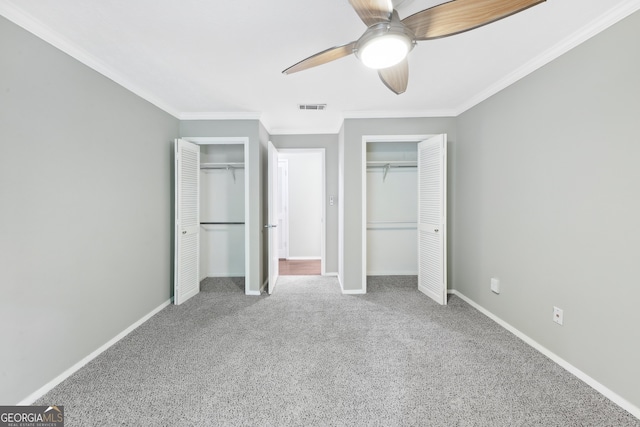 unfurnished bedroom with ceiling fan, carpet flooring, crown molding, and multiple closets