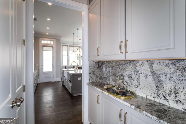 kitchen featuring dark wood-type flooring, white cabinetry, crown molding, light stone countertops, and decorative backsplash