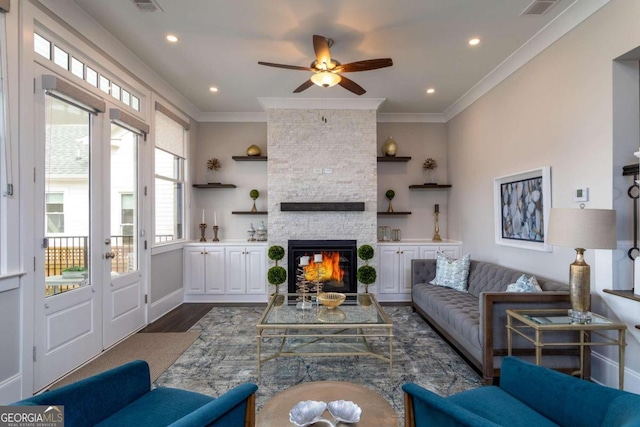 living room featuring ceiling fan, ornamental molding, dark hardwood / wood-style flooring, and a stone fireplace