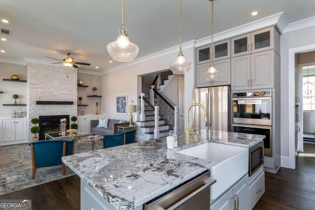 kitchen with dark wood-type flooring, a center island with sink, appliances with stainless steel finishes, pendant lighting, and a fireplace