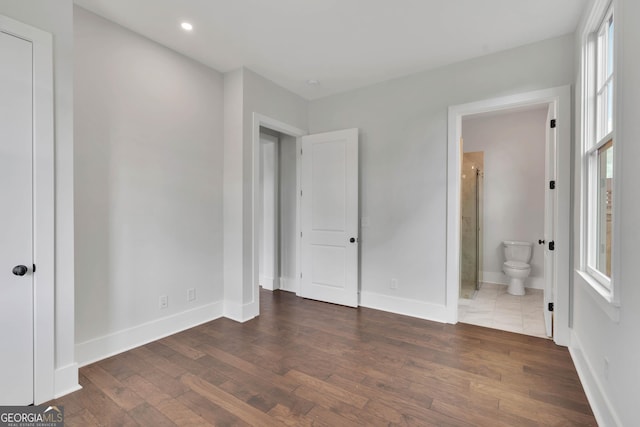 unfurnished bedroom with ensuite bathroom and dark wood-type flooring