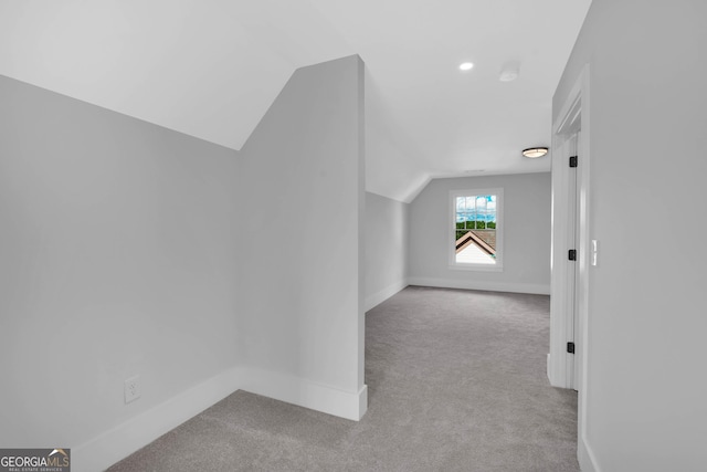 additional living space featuring vaulted ceiling and light colored carpet