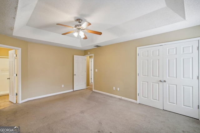 unfurnished bedroom featuring ceiling fan, light colored carpet, a textured ceiling, and a tray ceiling