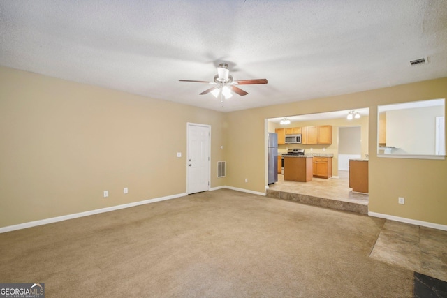 unfurnished living room featuring light carpet, ceiling fan, and a textured ceiling