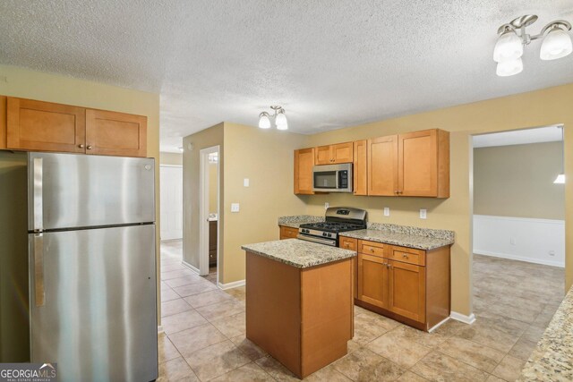 kitchen with light stone counters, a center island, stainless steel appliances, and a textured ceiling