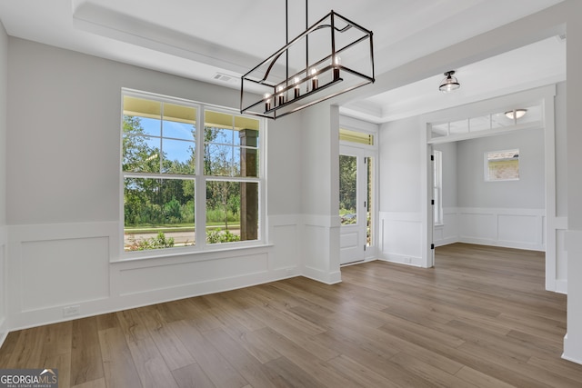 unfurnished dining area featuring light hardwood / wood-style flooring, a tray ceiling, and a healthy amount of sunlight