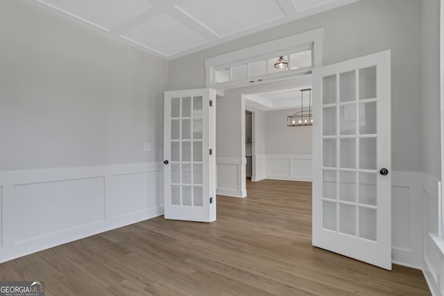 spare room with french doors, an inviting chandelier, and hardwood / wood-style floors