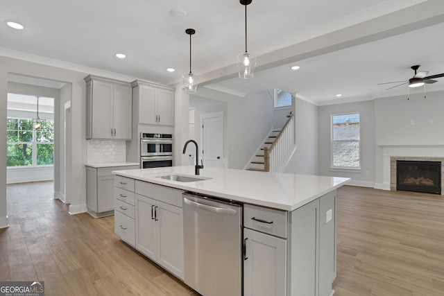 kitchen with stainless steel appliances, ceiling fan, light hardwood / wood-style flooring, a kitchen island with sink, and sink