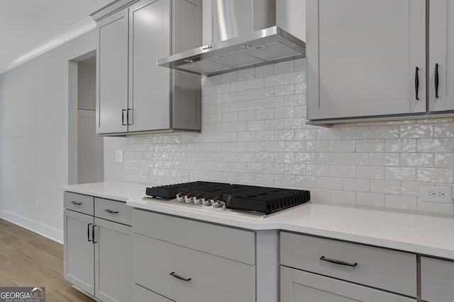 kitchen featuring gas stovetop, wall chimney exhaust hood, light hardwood / wood-style flooring, and tasteful backsplash