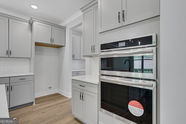 kitchen featuring gray cabinetry, light hardwood / wood-style floors, double oven, and tasteful backsplash