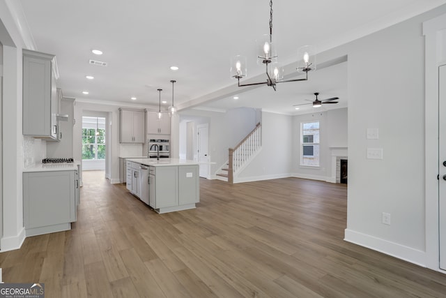 kitchen with an island with sink, tasteful backsplash, decorative light fixtures, light hardwood / wood-style flooring, and ceiling fan with notable chandelier