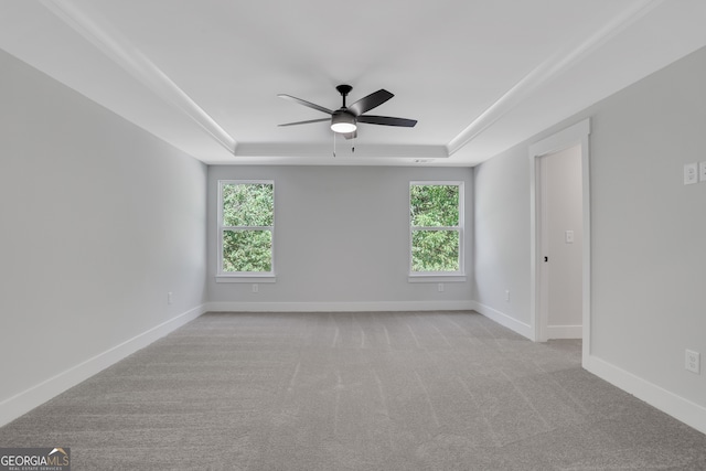 carpeted spare room with ceiling fan, a raised ceiling, and a healthy amount of sunlight