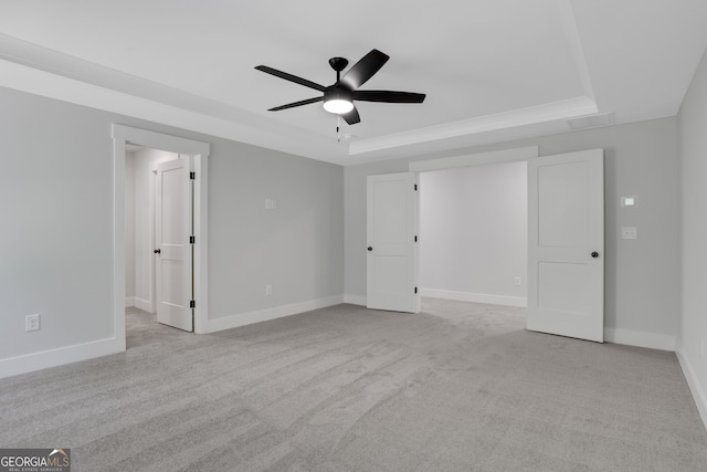 unfurnished bedroom featuring ceiling fan, a raised ceiling, and light carpet