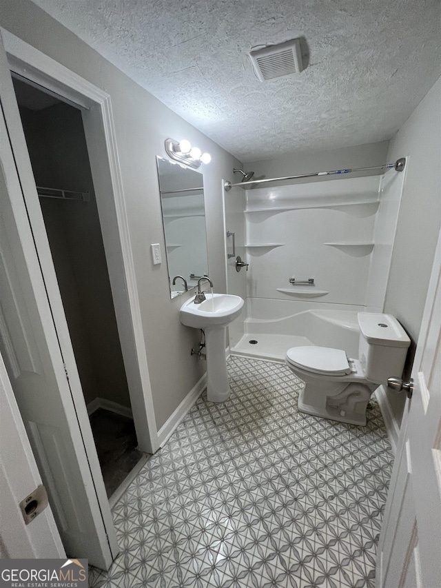 bathroom with a textured ceiling, toilet, and walk in shower