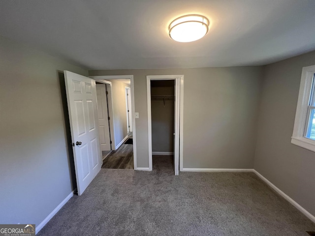 unfurnished bedroom with a spacious closet, a closet, and dark carpet