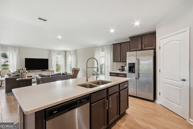 kitchen featuring sink, dark brown cabinets, appliances with stainless steel finishes, a kitchen island with sink, and light hardwood / wood-style floors