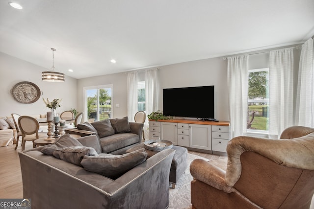 living room with vaulted ceiling, plenty of natural light, an inviting chandelier, and light hardwood / wood-style floors