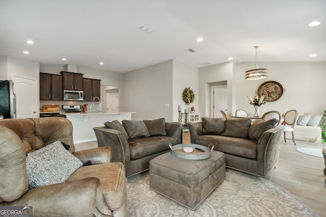 living room with lofted ceiling, sink, and light hardwood / wood-style flooring