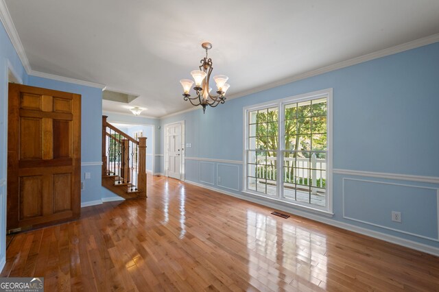 empty room with crown molding, hardwood / wood-style floors, and an inviting chandelier