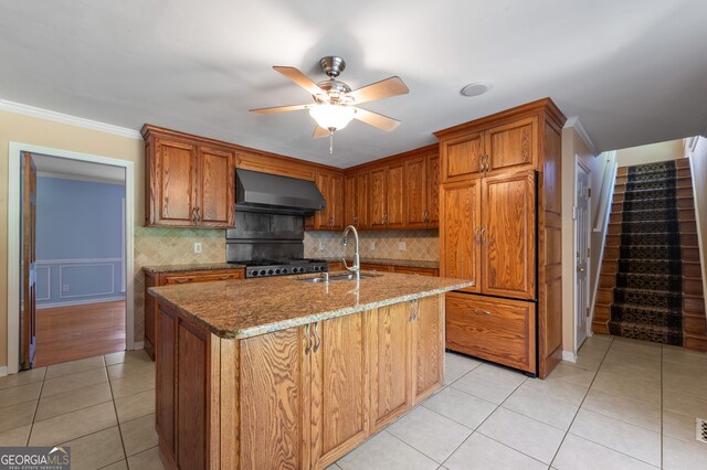 kitchen featuring wall chimney exhaust hood, tasteful backsplash, sink, a center island with sink, and light tile patterned flooring