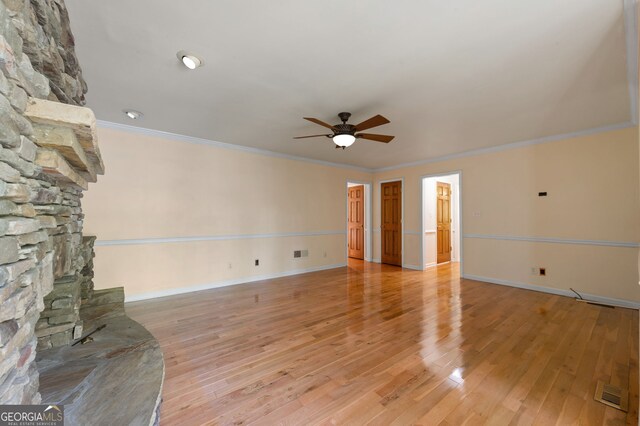 unfurnished living room with ceiling fan, light wood-type flooring, ornamental molding, and a stone fireplace