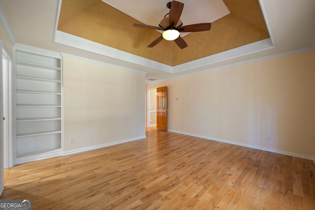 unfurnished room with light hardwood / wood-style flooring, ceiling fan, a raised ceiling, and built in shelves