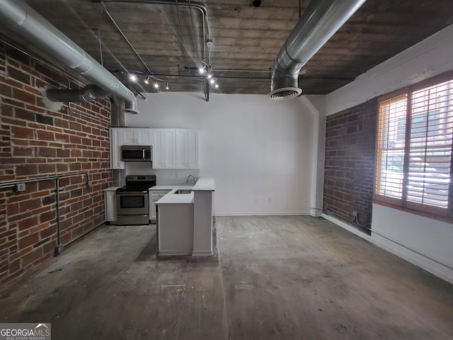 kitchen featuring white cabinets, sink, rail lighting, stainless steel appliances, and brick wall