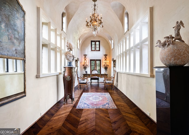 corridor featuring dark parquet flooring, a towering ceiling, and an inviting chandelier