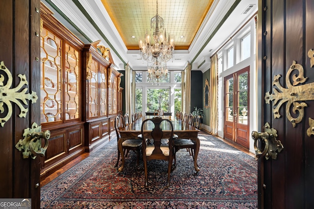 dining space featuring an inviting chandelier, wood-type flooring, a raised ceiling, and crown molding