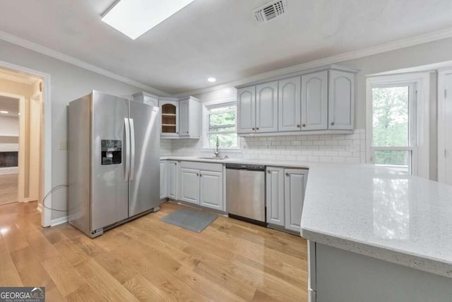 kitchen featuring appliances with stainless steel finishes, backsplash, ornamental molding, light wood-type flooring, and gray cabinets