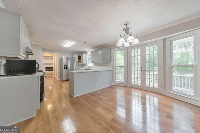 kitchen featuring light wood-type flooring, stainless steel fridge with ice dispenser, backsplash, ornamental molding, and kitchen peninsula