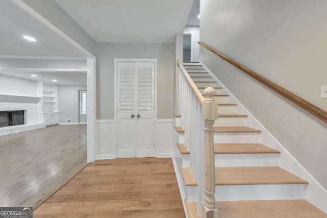 staircase with a fireplace, built in features, and light wood-type flooring