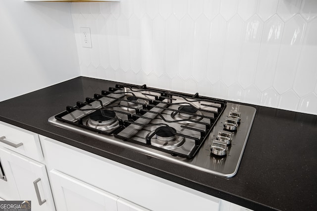 interior details with tasteful backsplash, white cabinetry, and stainless steel gas cooktop