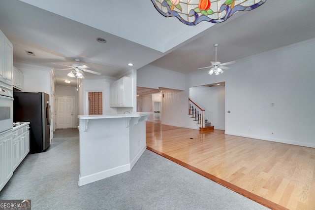 kitchen with ceiling fan, light hardwood / wood-style flooring, white cabinets, a kitchen bar, and kitchen peninsula