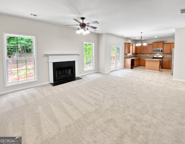 unfurnished living room featuring ceiling fan with notable chandelier, light colored carpet, plenty of natural light, and sink