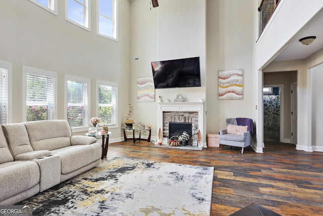 living room featuring dark hardwood / wood-style flooring, a towering ceiling, a stone fireplace, and ceiling fan