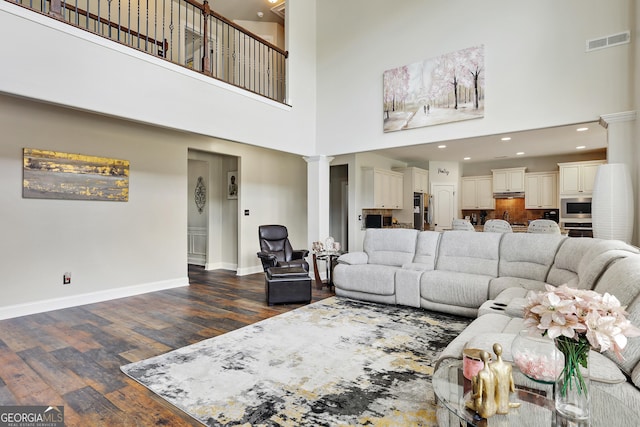 living room with ornate columns, dark wood-type flooring, and a high ceiling